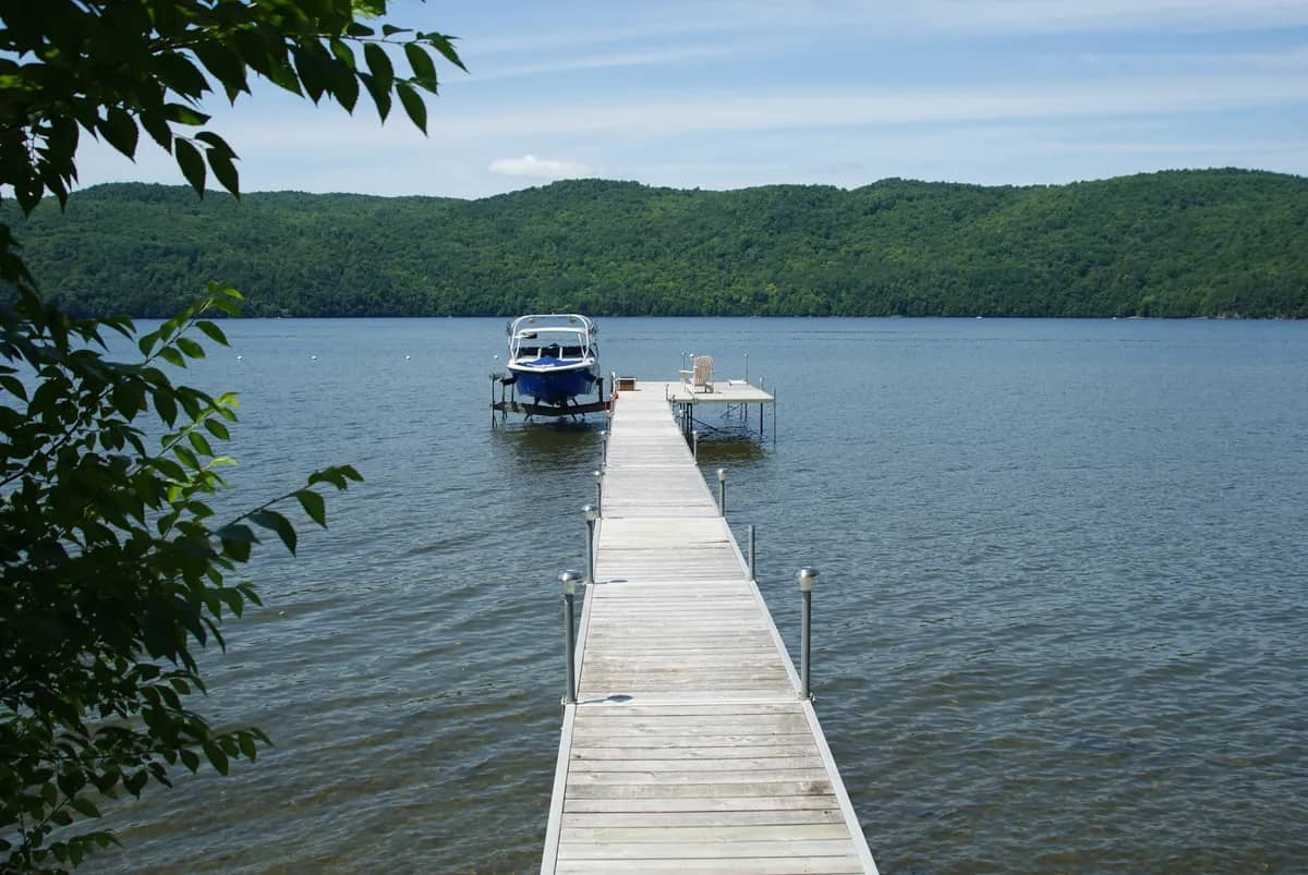 Boat raised on a lift at the end of a dock, wooded lakeshore